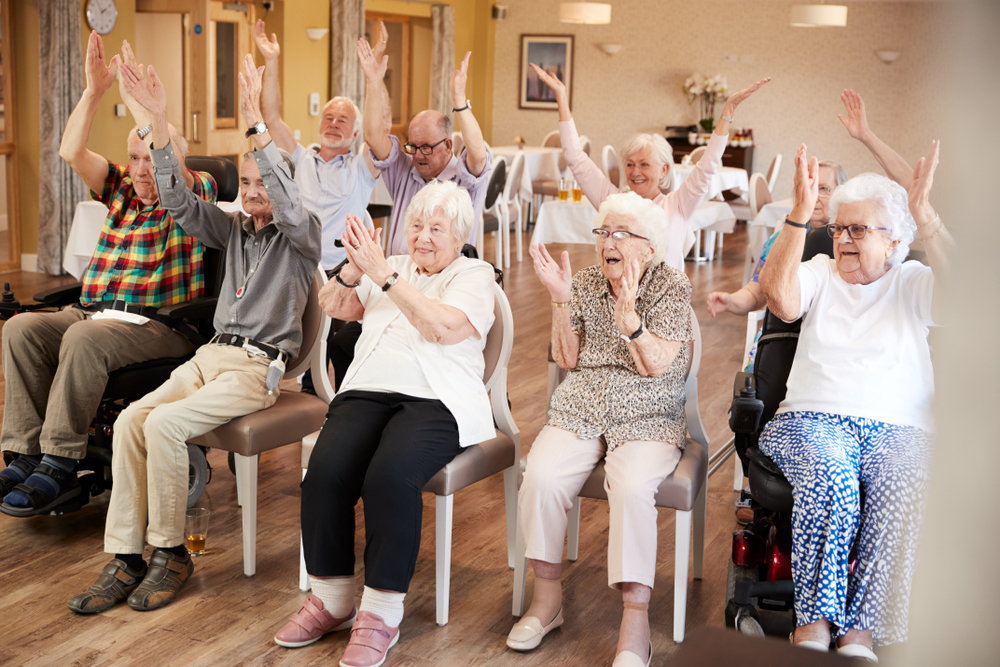 Carer Leading Group Of Seniors In Fitness Class In Retirement Home